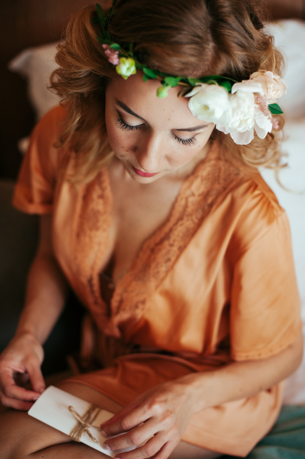 A red-haired girl in a wreath of flowers, dressed in an orange dressing gown, holds a postcard tied with a ribbon.