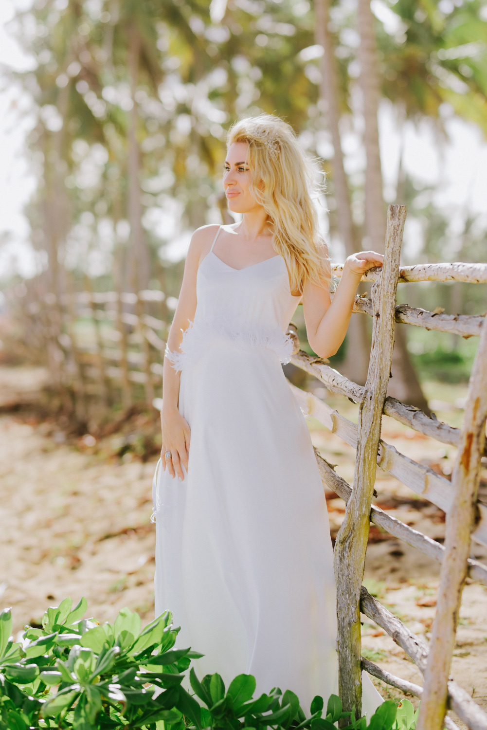 Bride at a wooden fence on the background of palm trees.