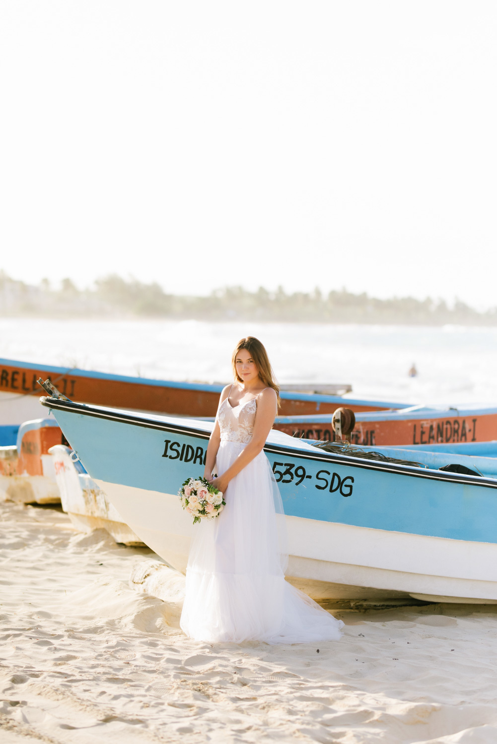 the woman (bride) with a wedding bouquet in a white wedding dress posing by a wooden boat on the beach