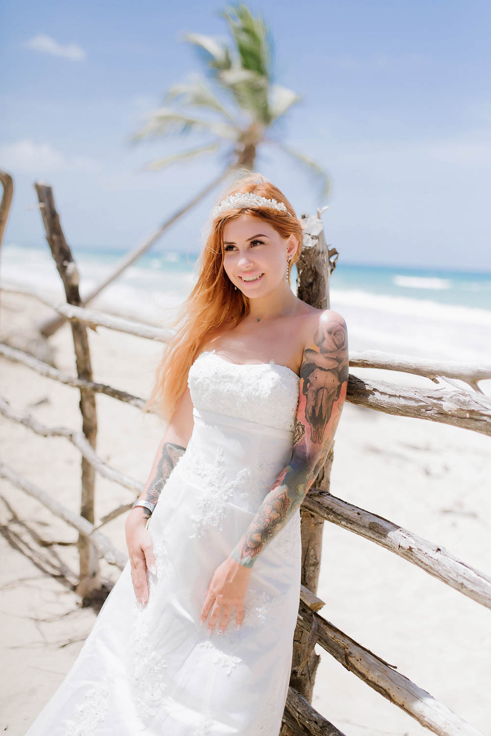 The bride leaned on a wooden fence with a tilted palm tree and the sea in the background.