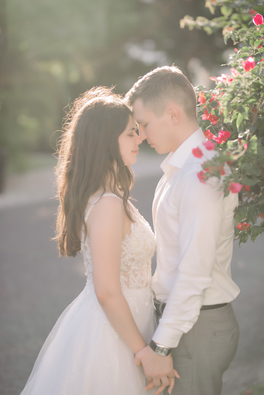 By a shrub of crimson flowers, the bride and groom leaned their heads together, holding hands.