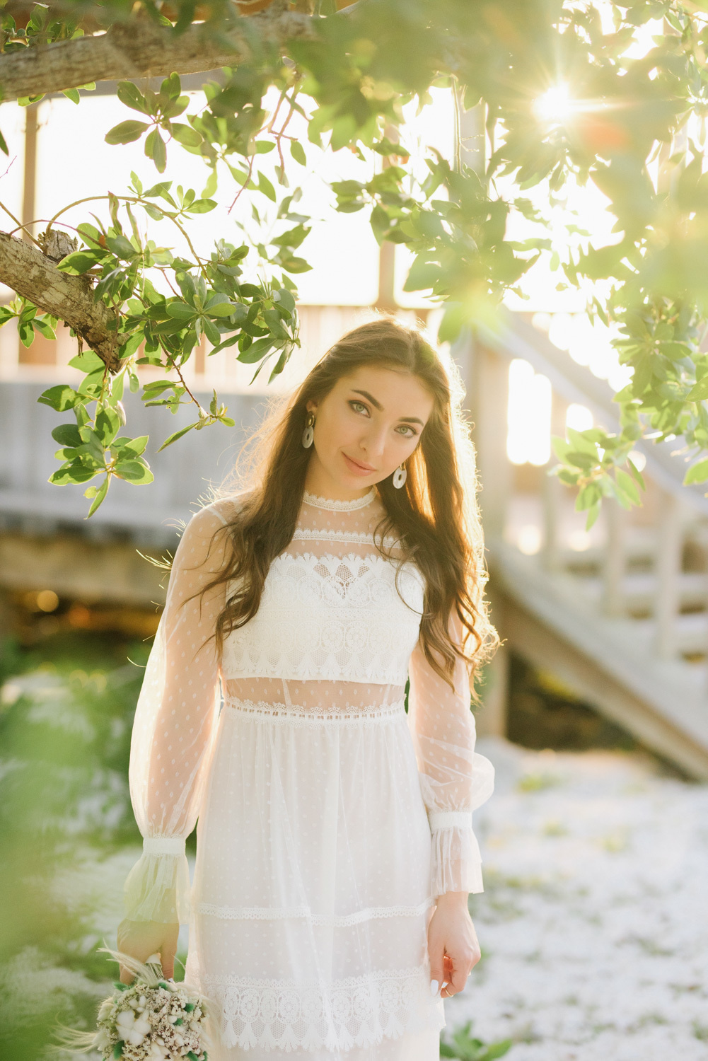 Bride in a white dress on the background of a white wooden staircase and green trees.