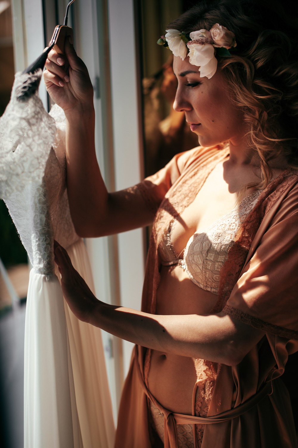 A girl at the window looks at a wedding dress in the sunlight.