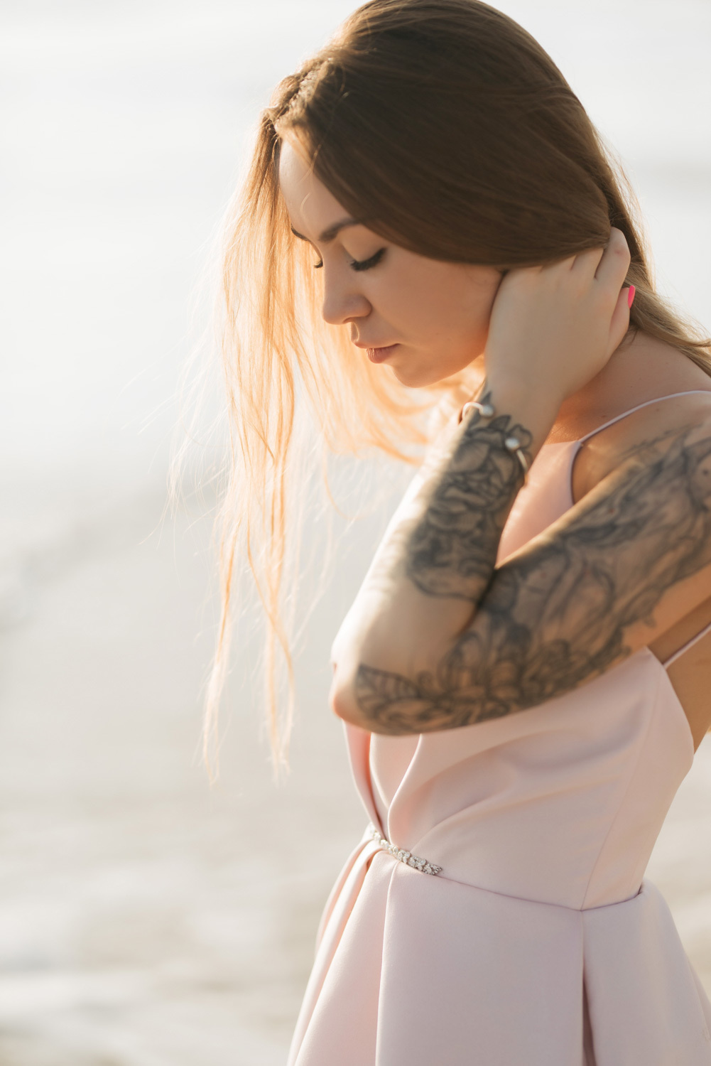 A bride in a pink wedding dress looks at the sea sand.