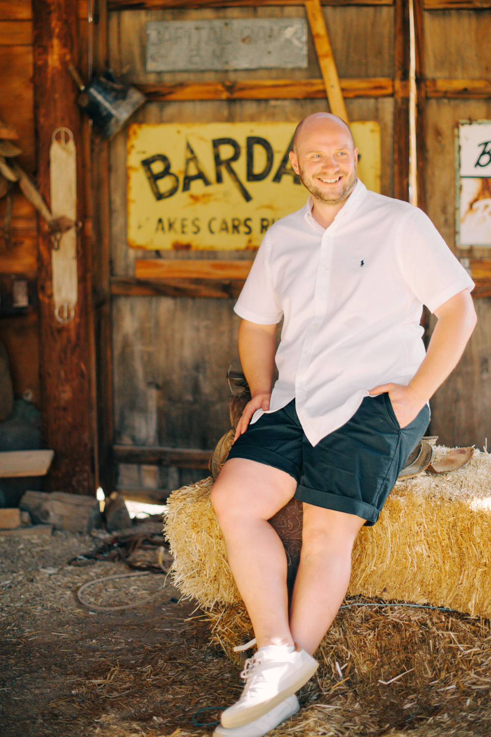 Жених сидит на тюке соломы на фоне старинной вывески.