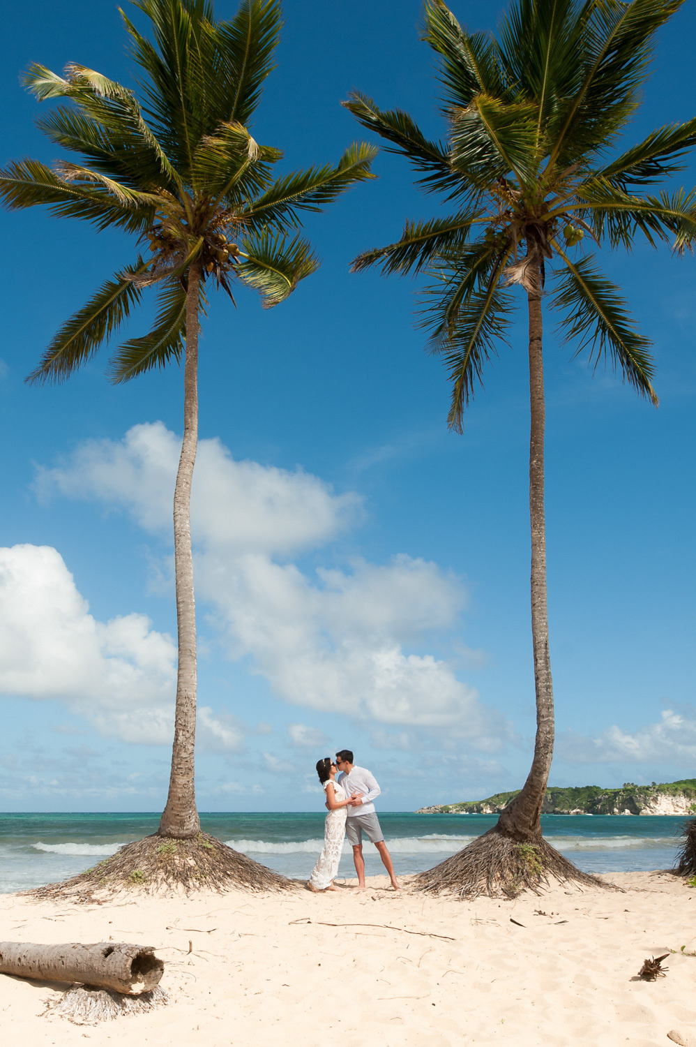 Silhouettes of the bride and groom among two tall palm trees on the background of the sea.