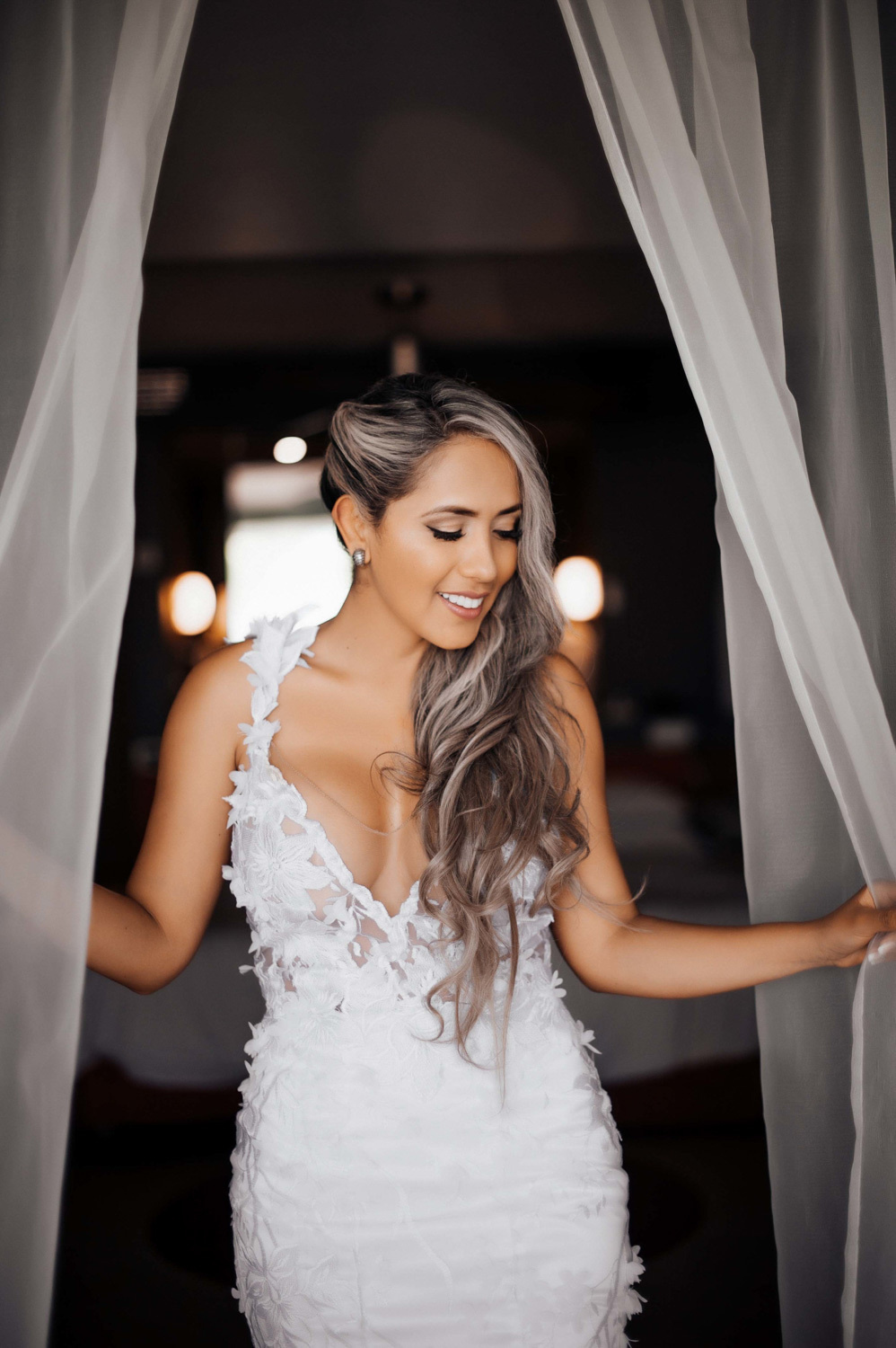 The bride stands with the curtains drawn back against a dark background.