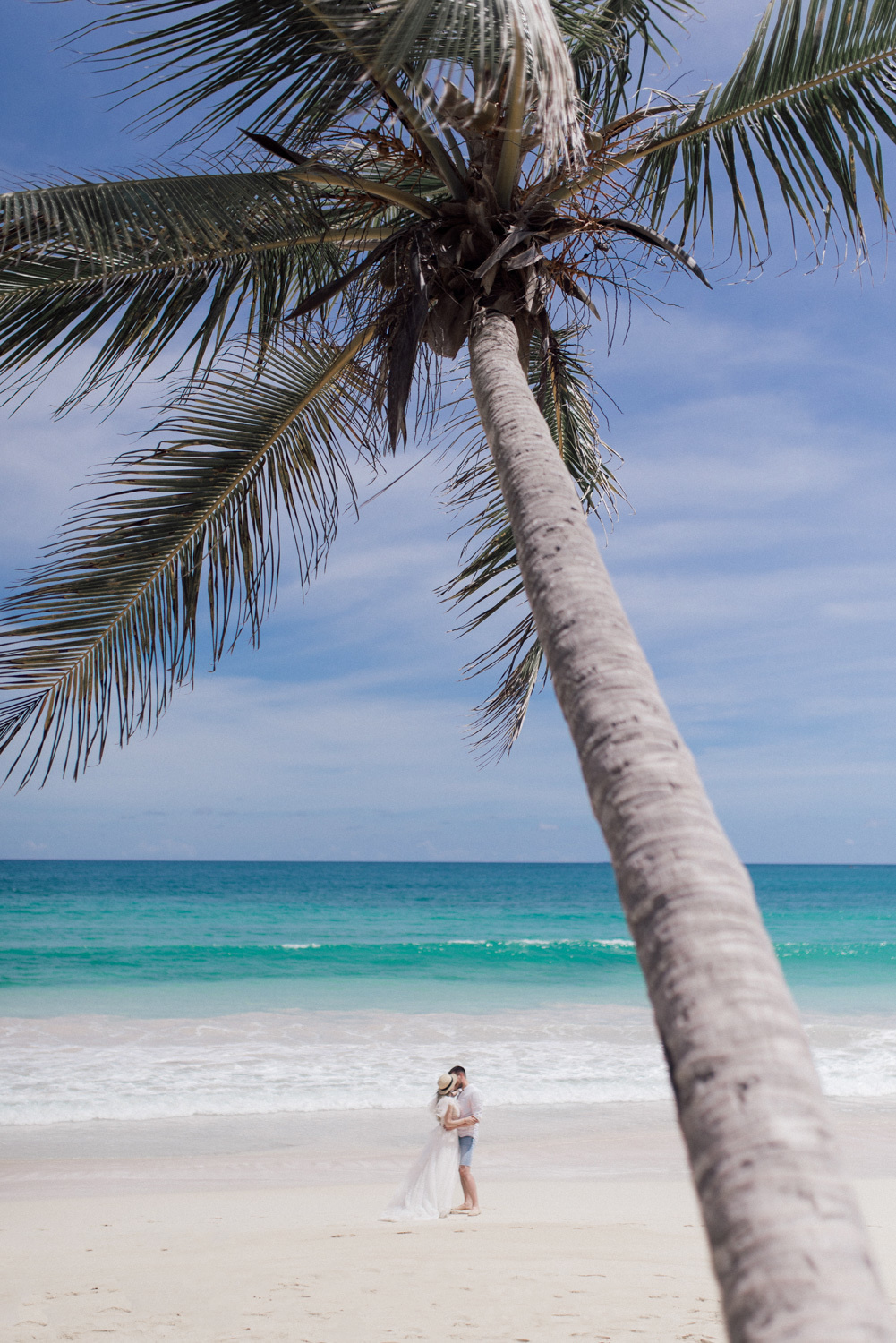 Bride and groom on a sandy beach with a tall palm tree on the sea background.