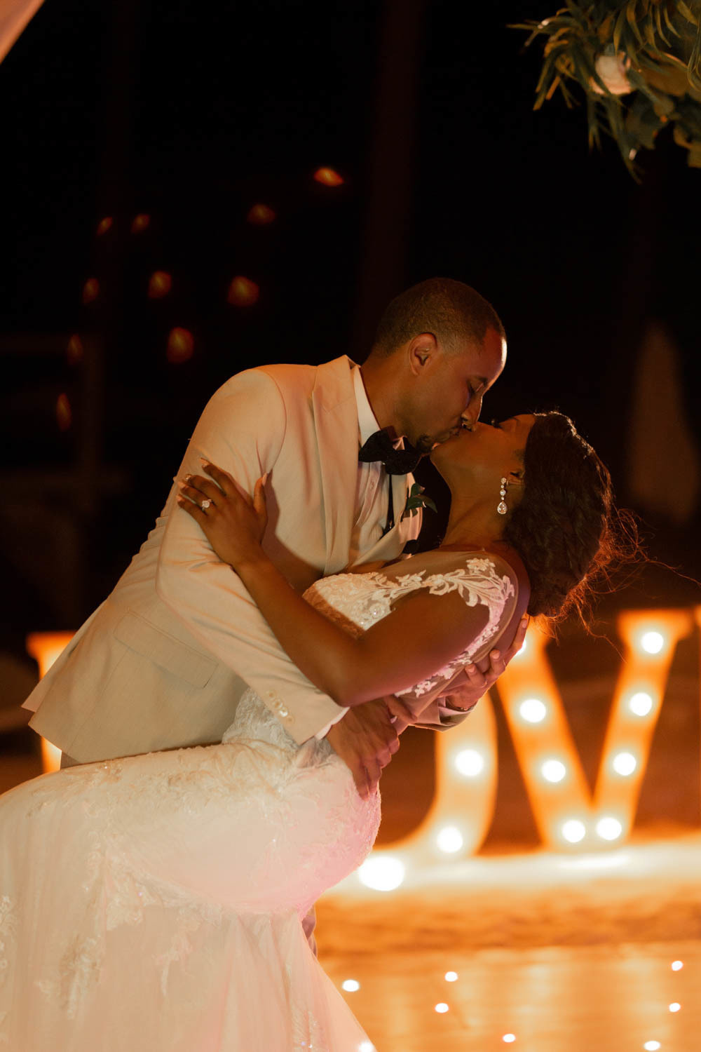 Against the background of bright lights, the groom kisses the bride, bending down to the ground.