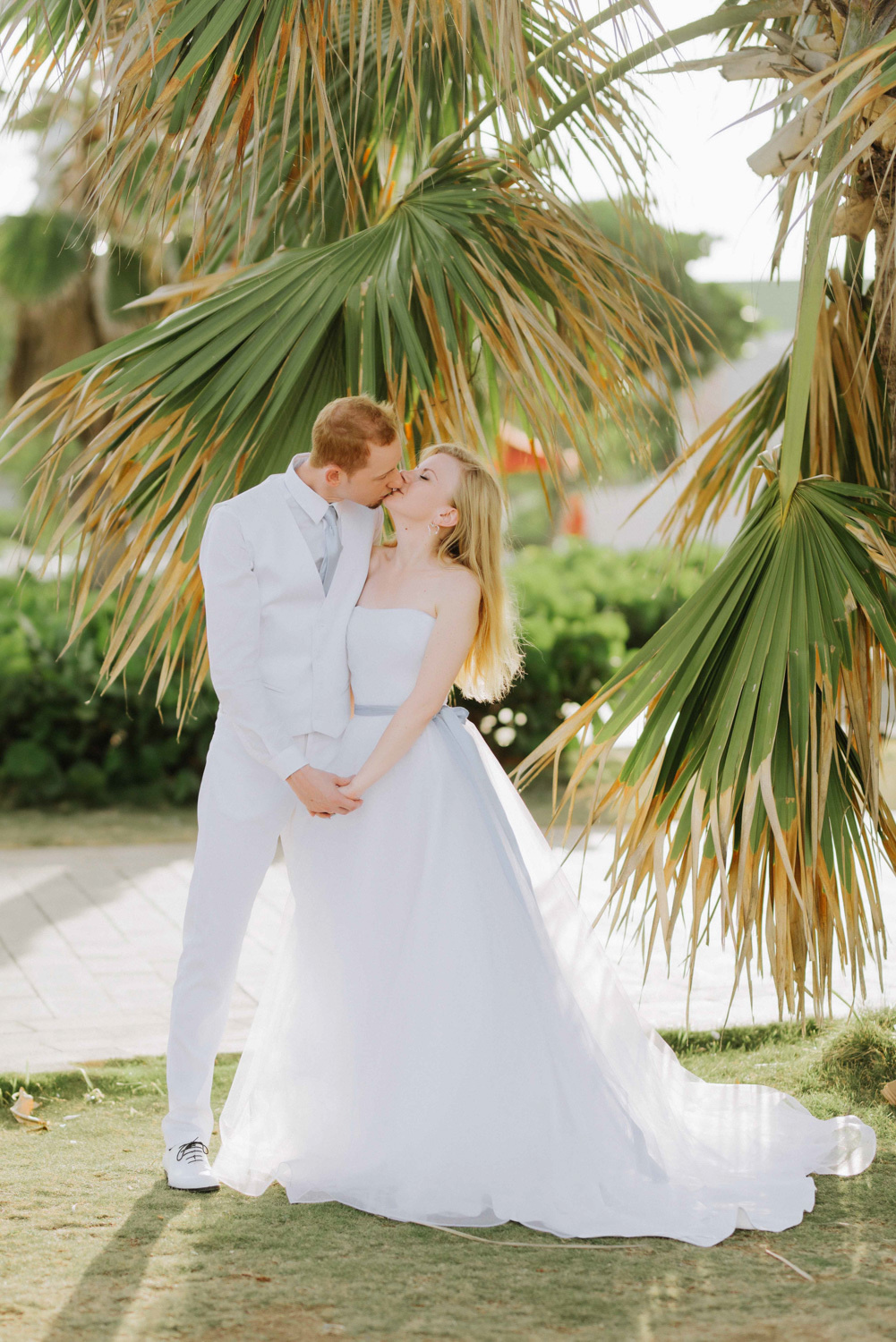 Жених и невеста целуются на фоне пальм.