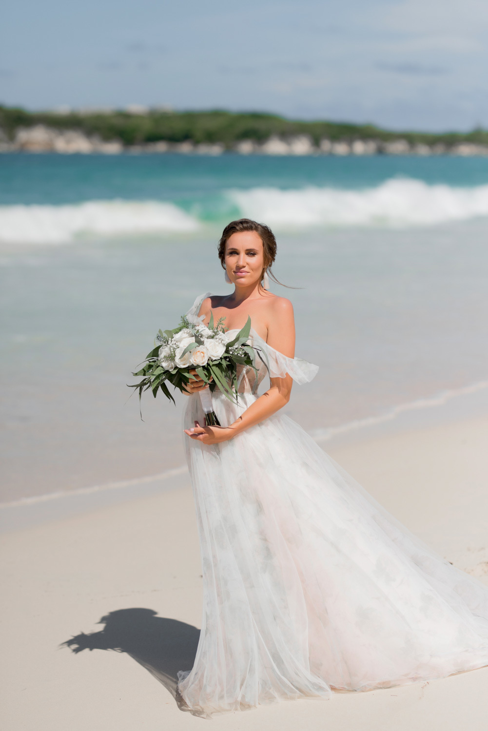 Невеста в белом платье с букетом белых цветов на фоне морского залива.