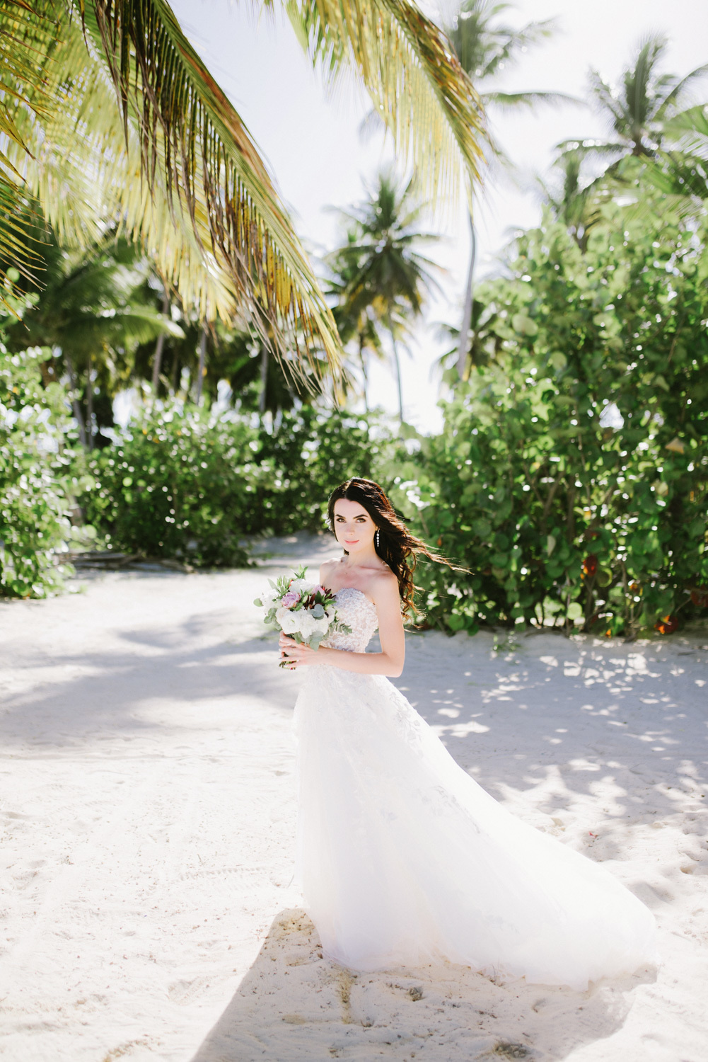 Невеста с букетом в руках на фоне пляжа с пальмами.