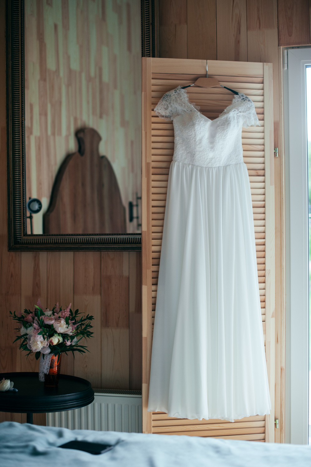 In the room, a long white dress hangs on the wooden shutters of the window.