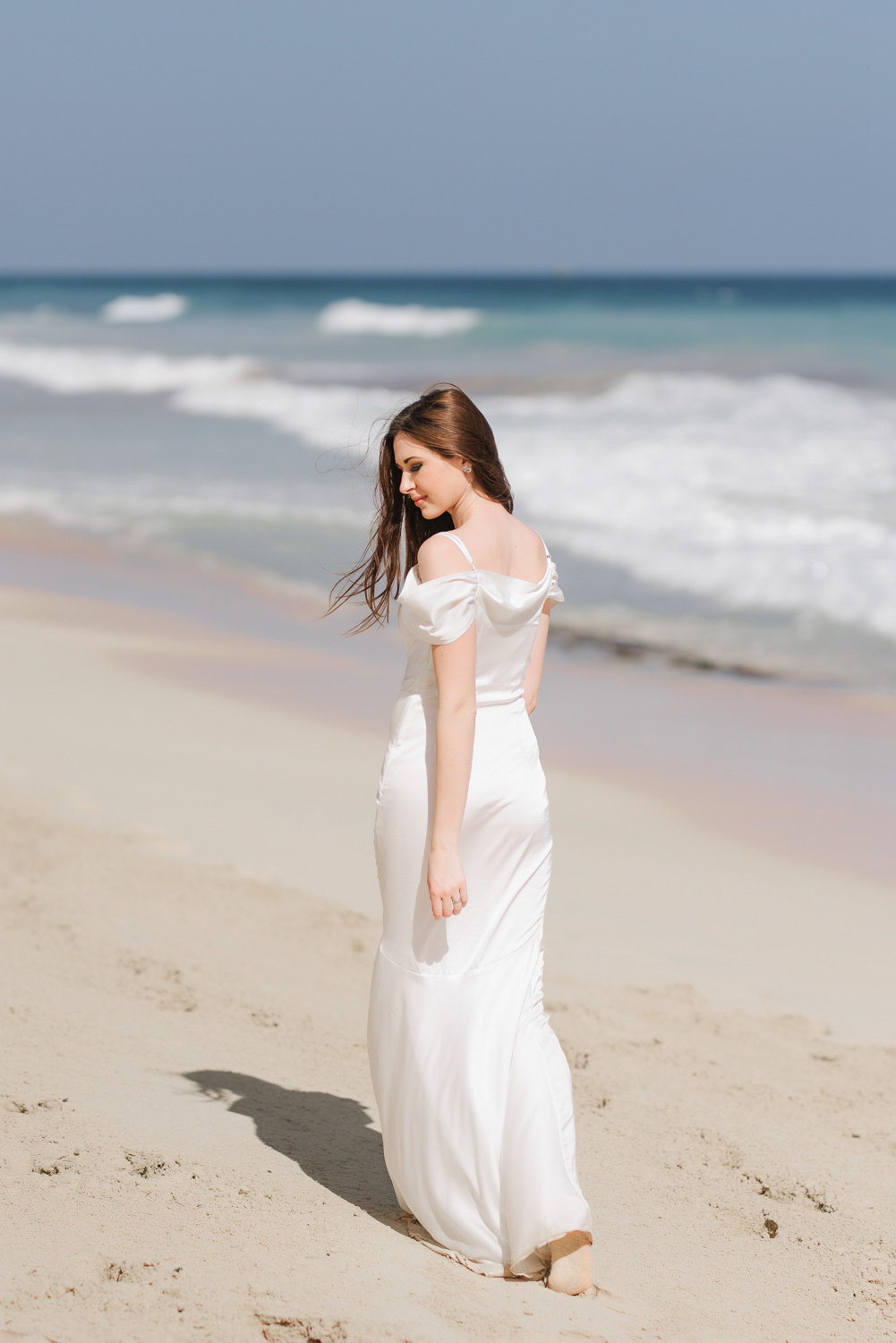 A bride in a white dress walks on the sand against the background of the sea.