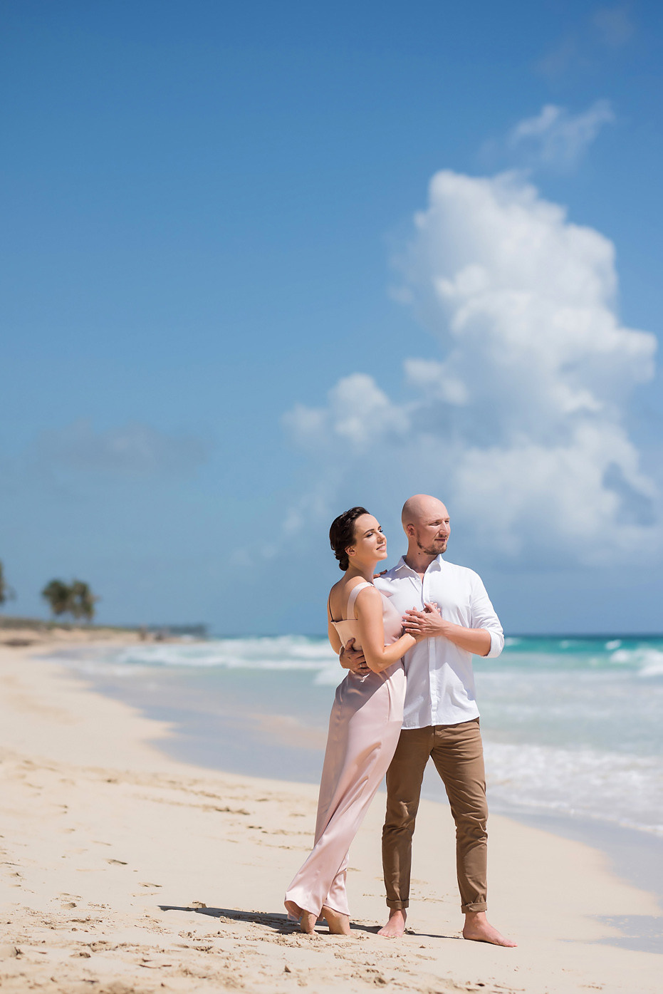 Жених держит невесту за руки на фоне океана и огромного белого облака.