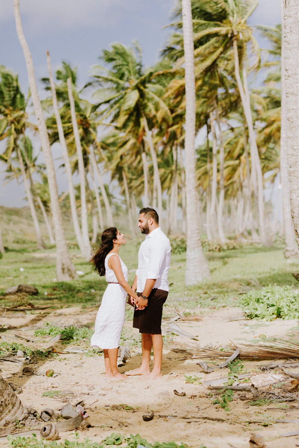Жених и невеста, взявшись за руки, смотрят друг другу в глаза на фоне пальм.