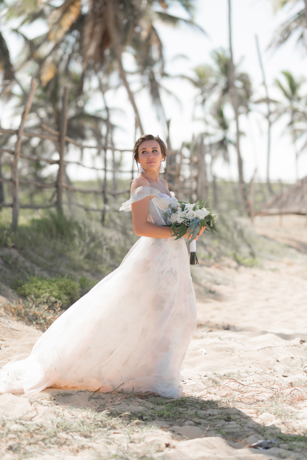 Невеста с букетом цветов на фоне пляжа с пальмами.