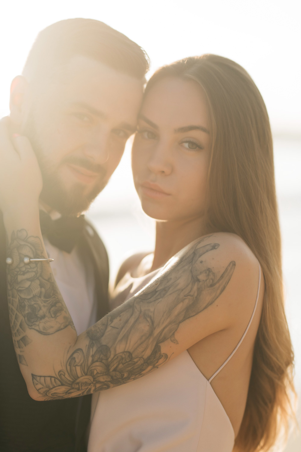 Faces of the bride and groom. The bride's tattooed arm hugs the groom's face.