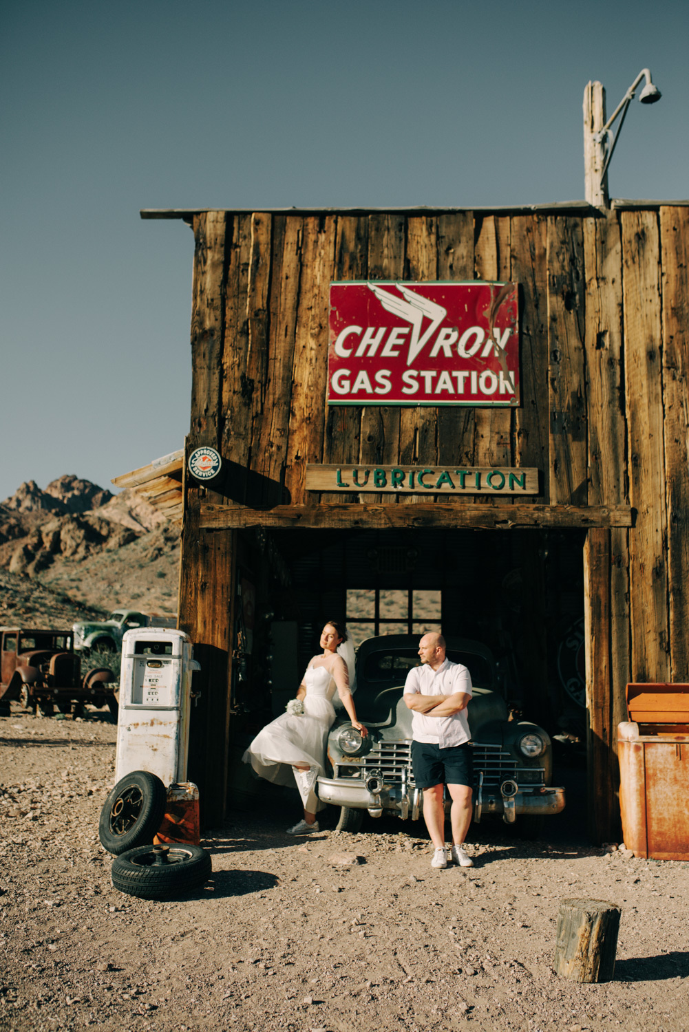Невеста с женихом стоят у заброшенной заправочной станции.