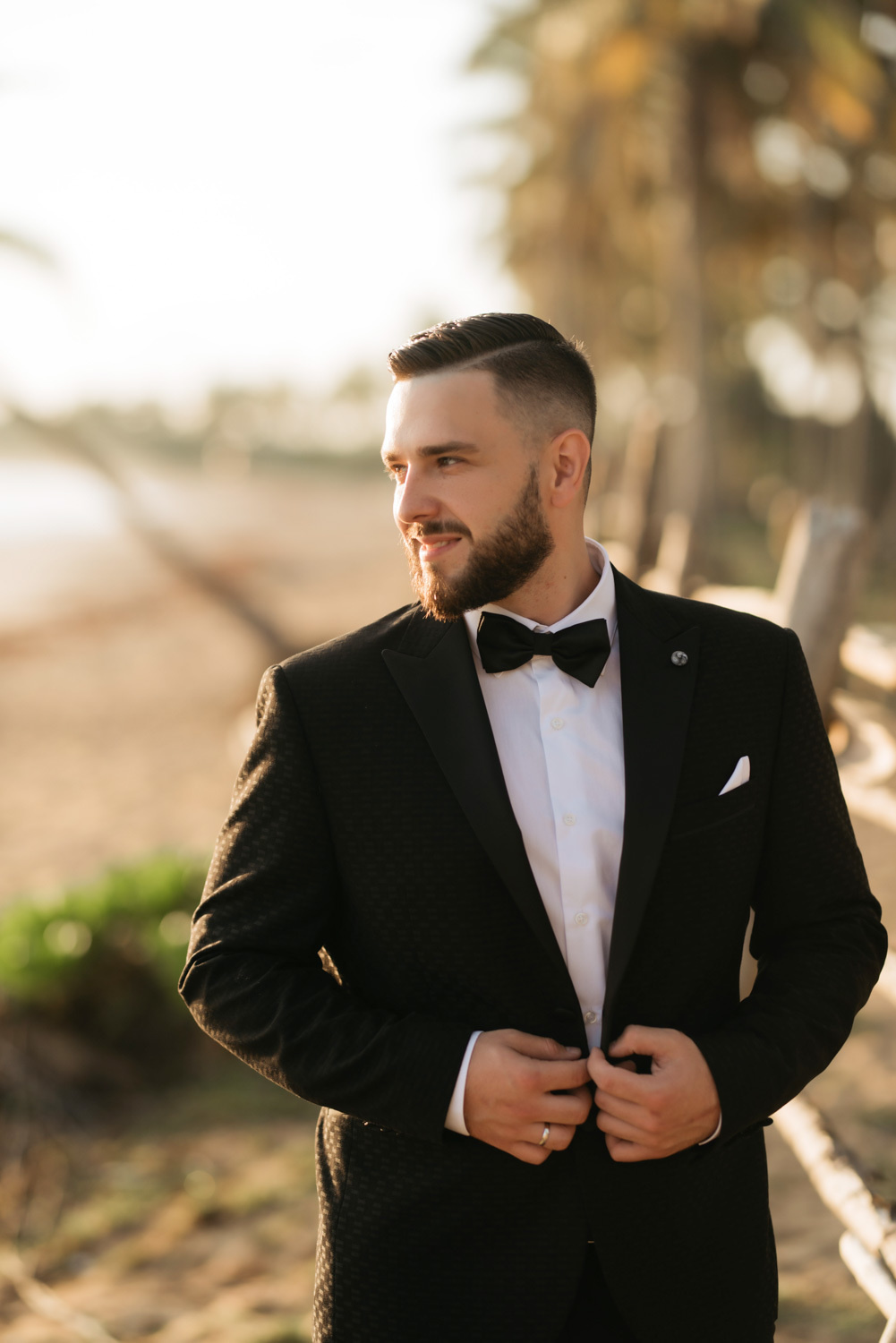 Groom in a dark wedding suit on the background of the sea coast with palm trees.