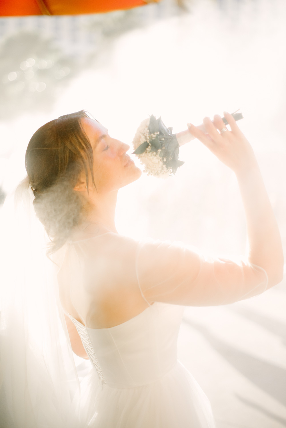 Невеста на улице, подняв букет вверх, нюхает цветы в дымке тумана.