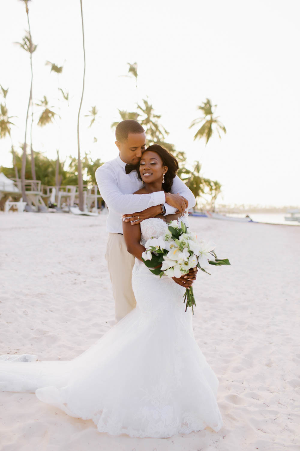 The groom embraces the bride on the background of a deserted beach with palm trees.