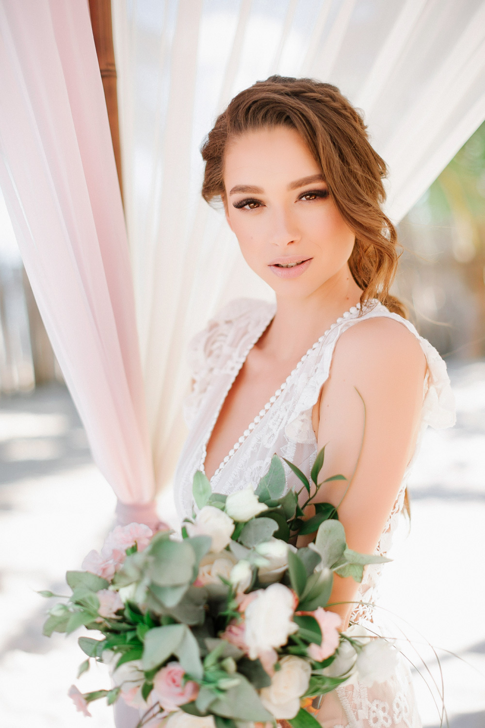 The bride's face with a bouquet of flowers on the background of pink and white curtains of the tent.