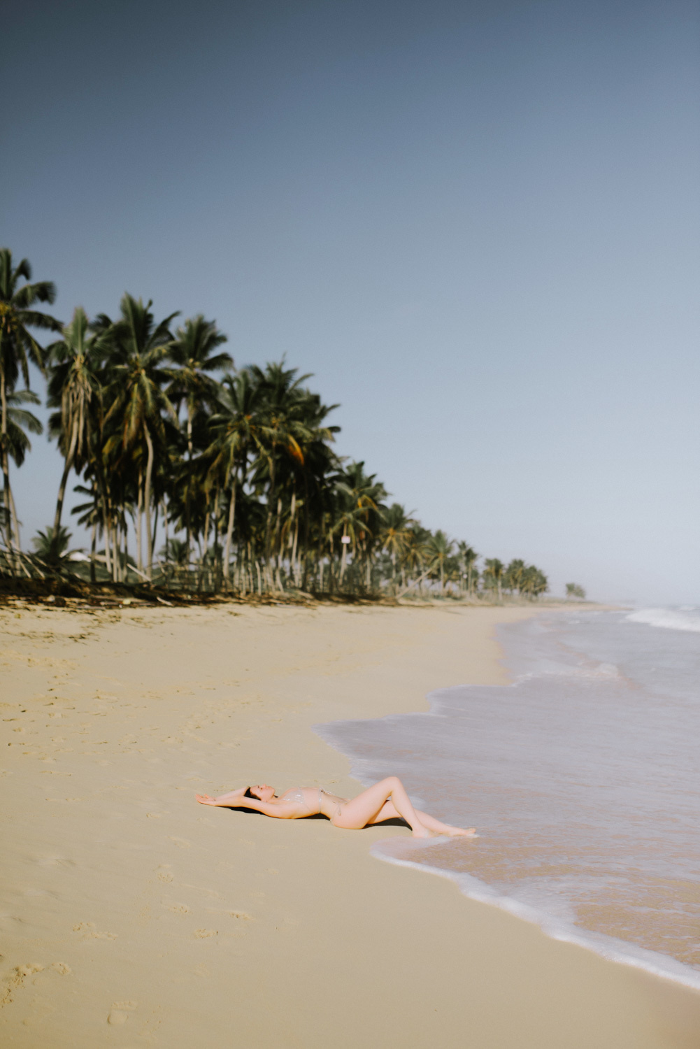 A bride in a bathing suit lies on the sand by the sea against the background of a beach with palm trees.