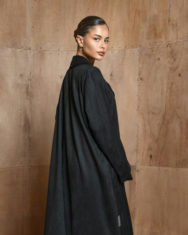 Lookbook portrait of a woman wearing a black coat beside a wood-textured wall