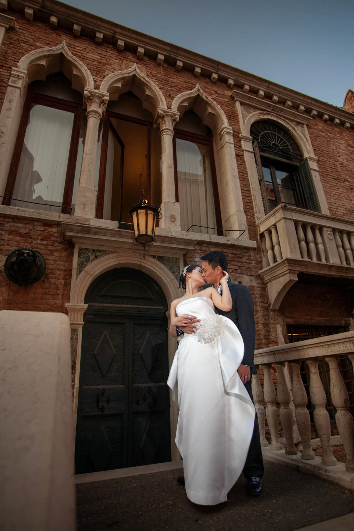 Partner kissing Thai bride from behind in historic Venetian Arsenal quarter.