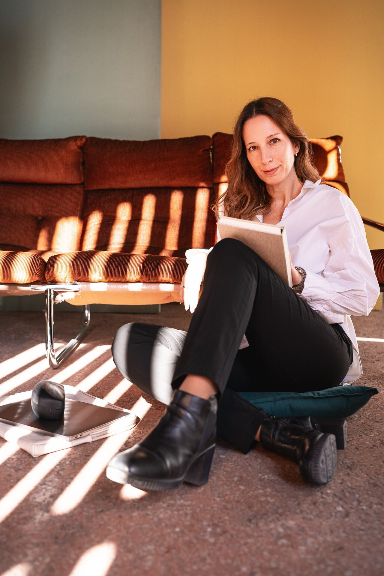 žena sedi na podu naslonjena na garnituru držeći rokovnik na kolenima