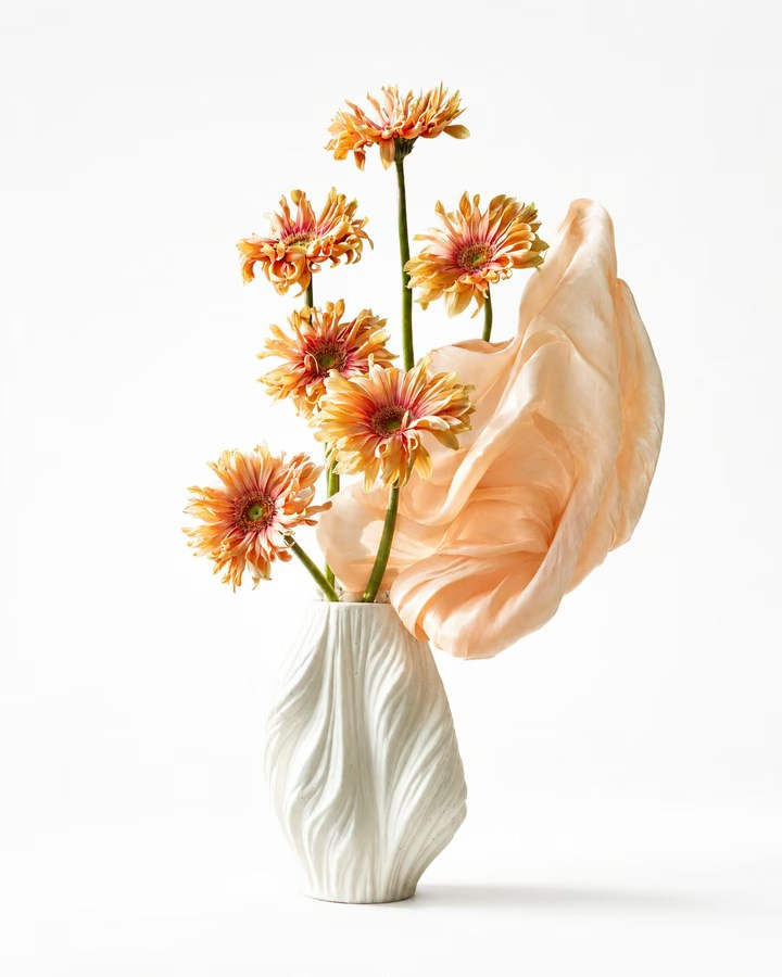 Orange flowers in a sculptural white vase held by a gloved hand