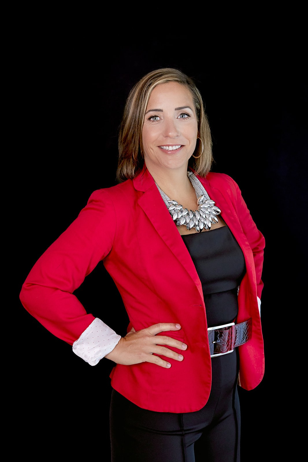 Headshot of woman in red blazer, brown hair and hands on hips 