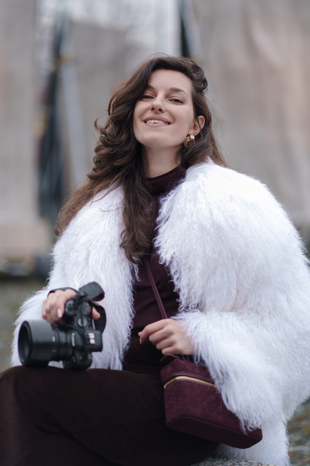 Woman holding camera wearing white fur jacket at Pitti Uomo 109 Florence