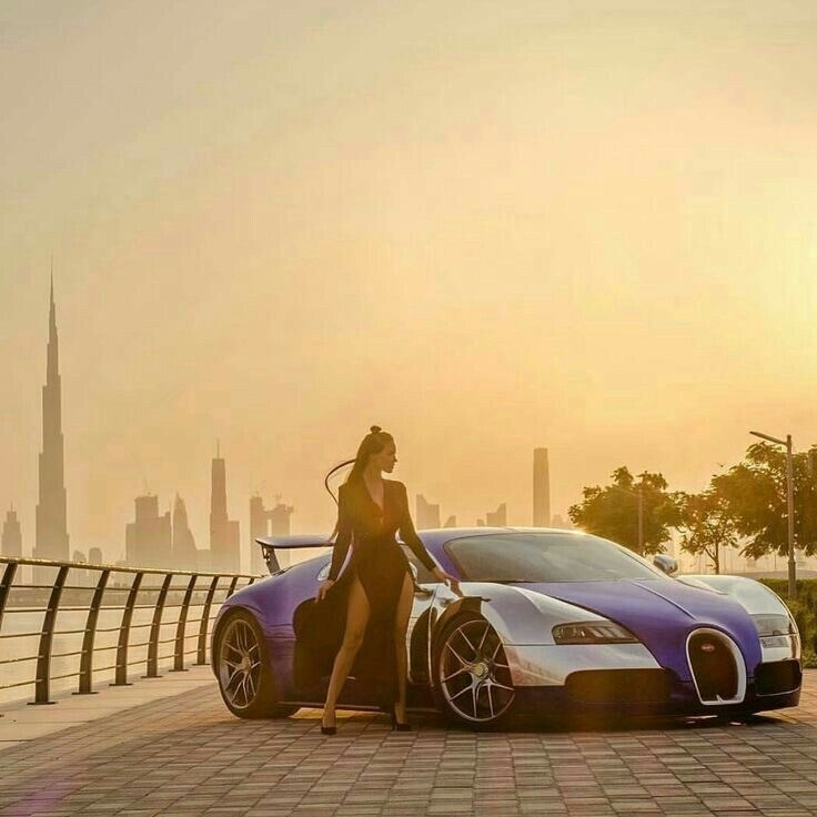 A model stands next to a beautiful expensive white and blue Bugatti car against the backdrop of Dubai's skyscrapers during a beautiful sunset