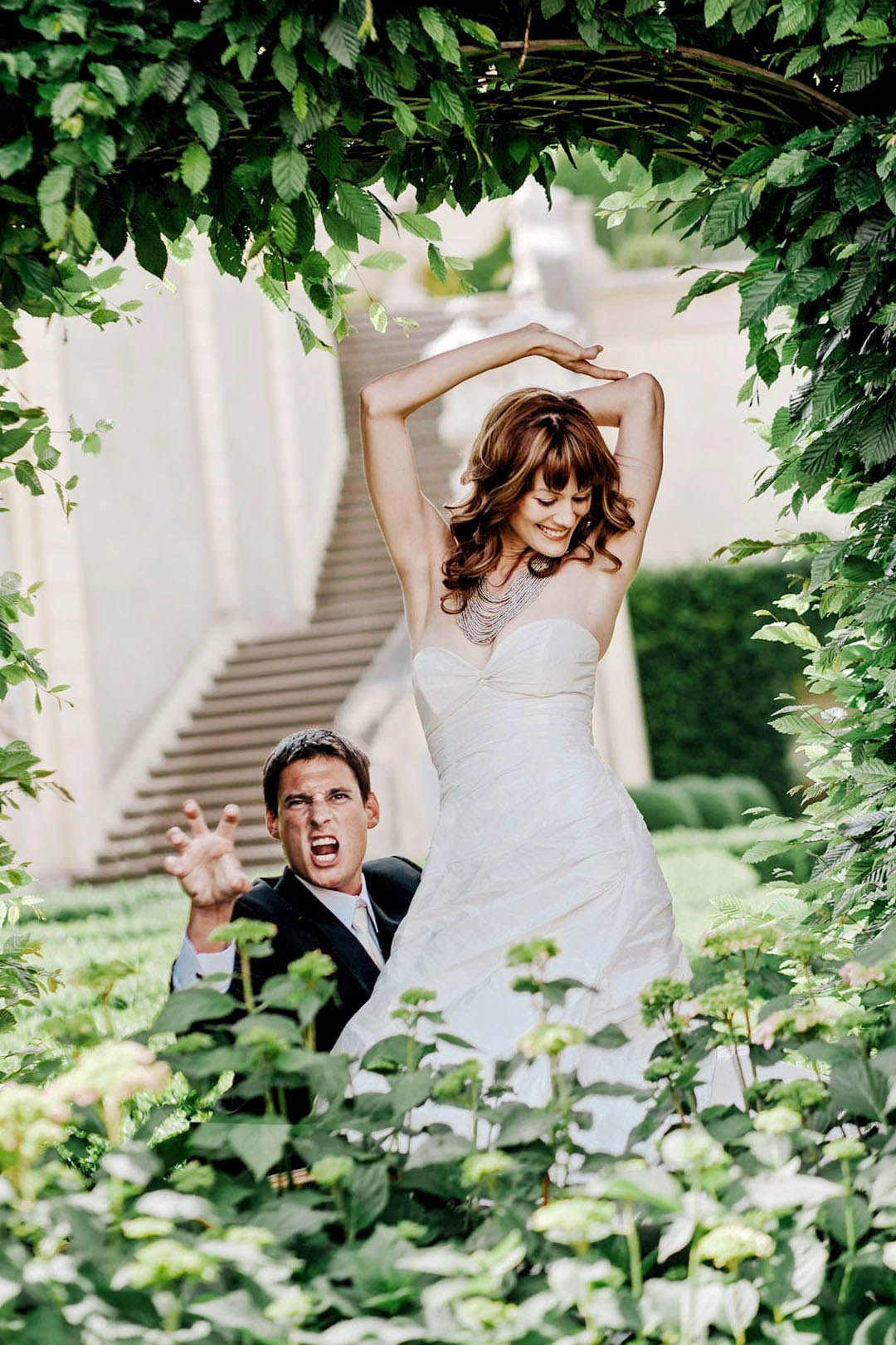 Groom making tiger gesture with red-haired bride posing in Vrtba Garden, Prague, destination wedding