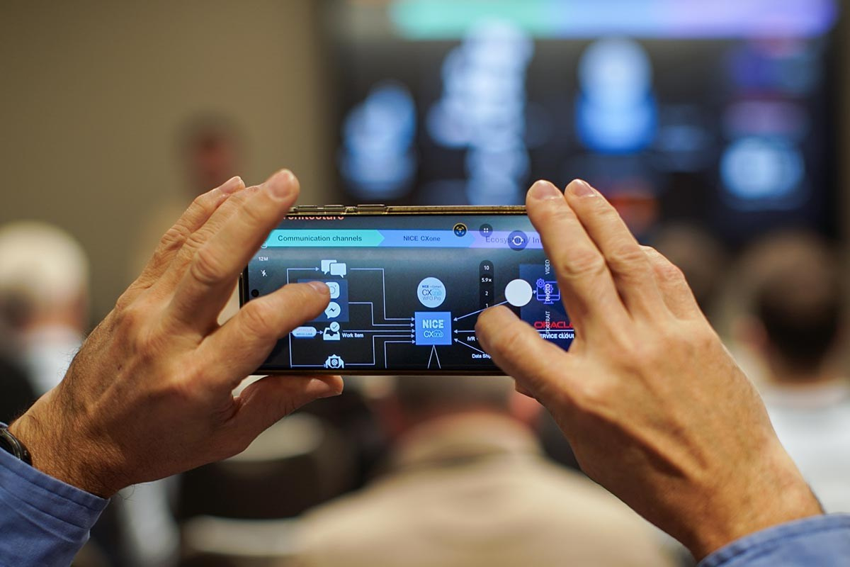Attendee photographing conference slide on phone during Orange Business Sales Kick-Off 2026 at Hilton Prague.