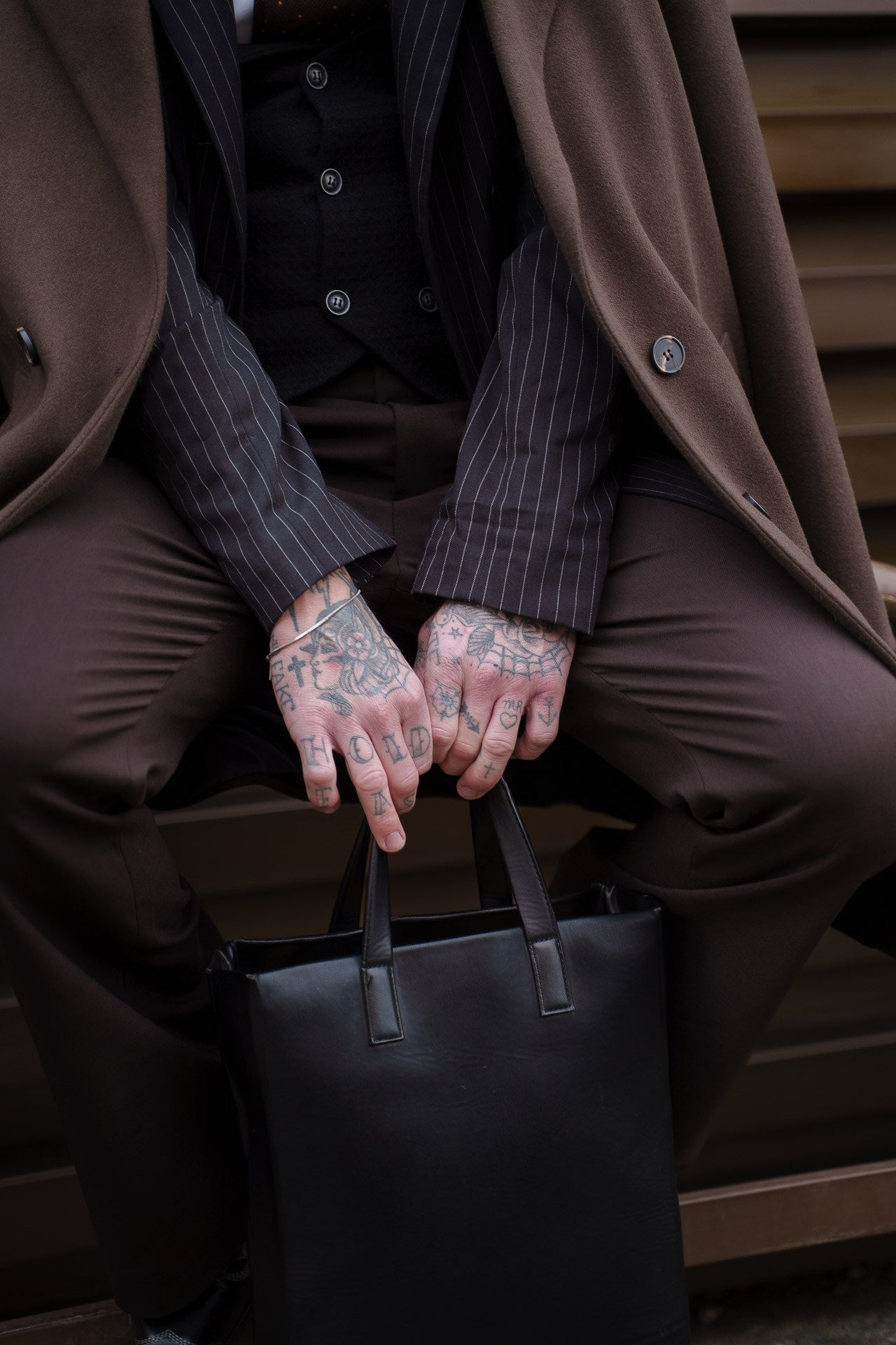 Close up of tattooed hands holding black leather bag at Pitti Uomo