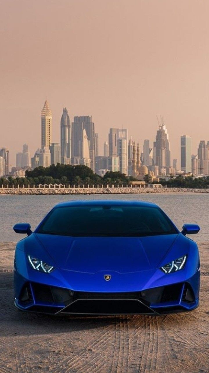 A blue Lamborghini with skyscrapers in the background during sunset in Dubai.