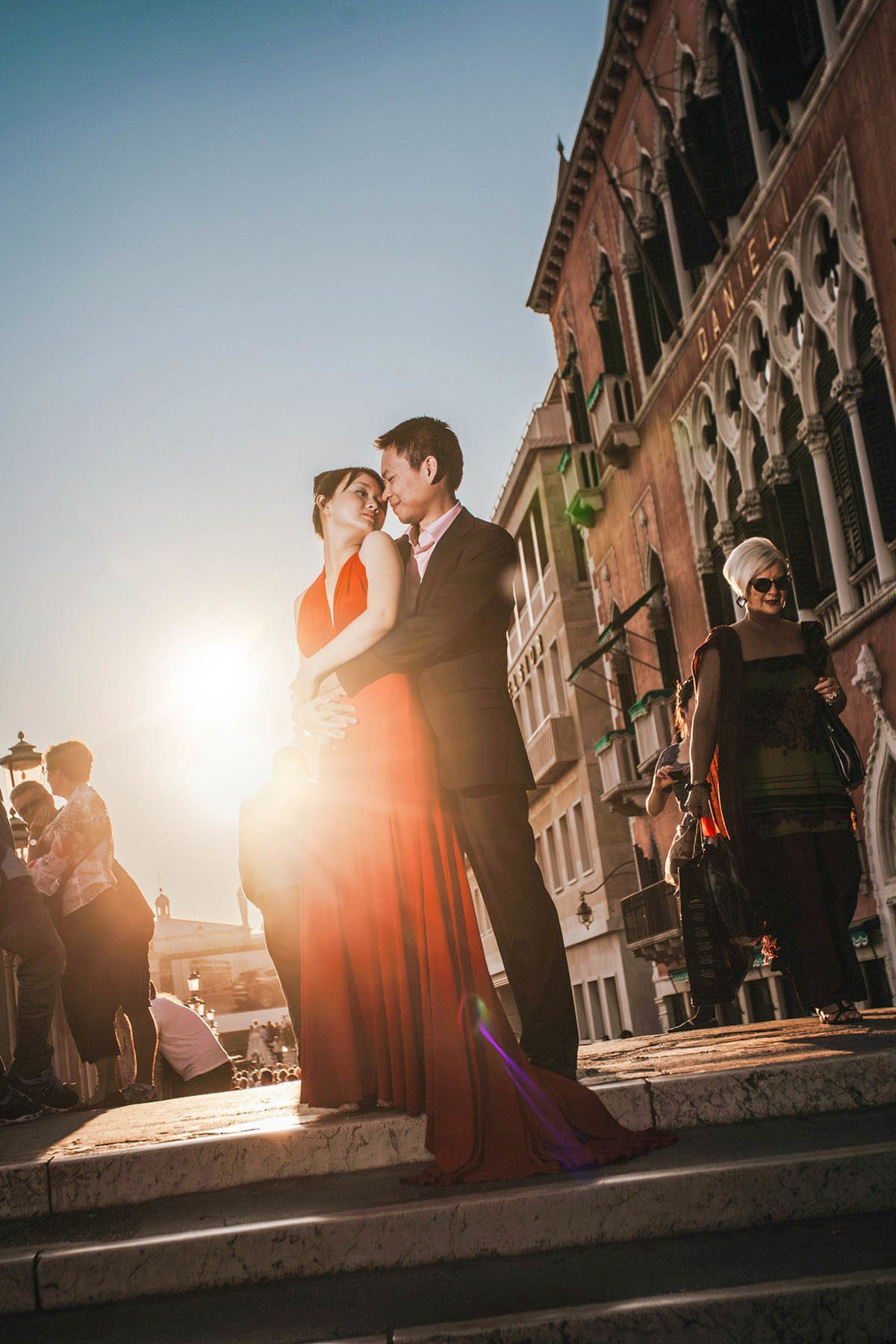 Thai couple embracing above canal with late evening sun flare near Hotel Danieli Venice.