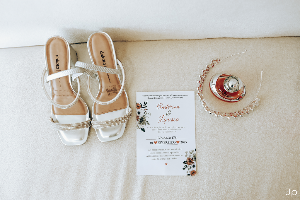 Um par de sapatos de noiva, um perfume, uma coroa e um cartão sobre um sofá.