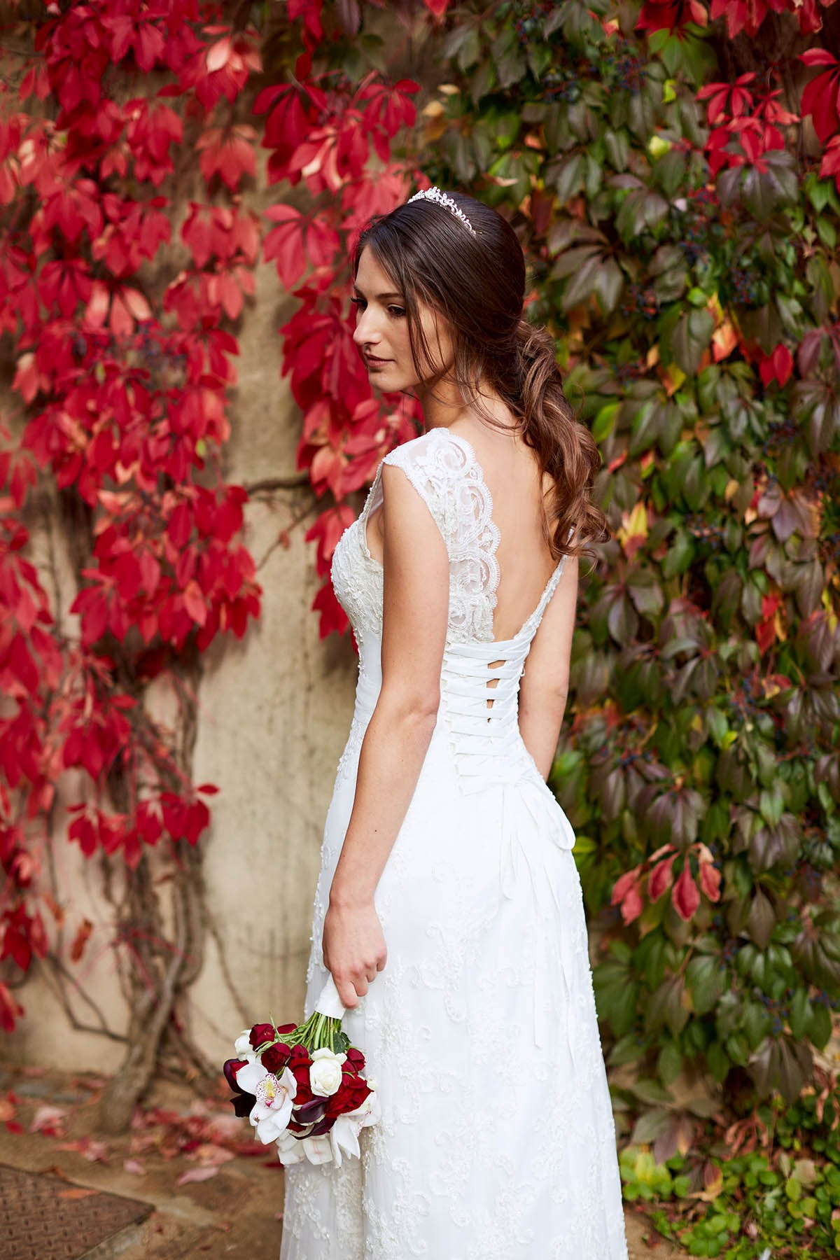 A Ukrainian bride is viewed from behind as she stands near a wall of red ivy at the Ledebour Garden in Prague.