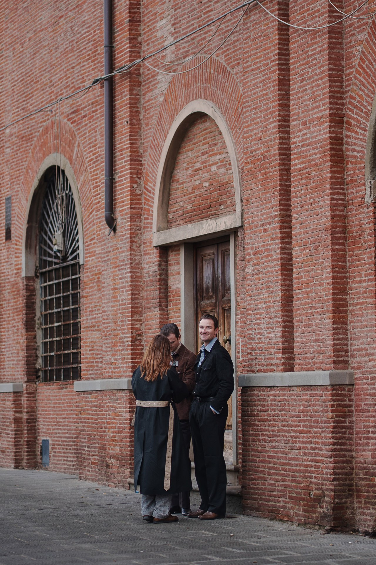Couple standing near historic brick building in Florence during Pitti Uomo street style