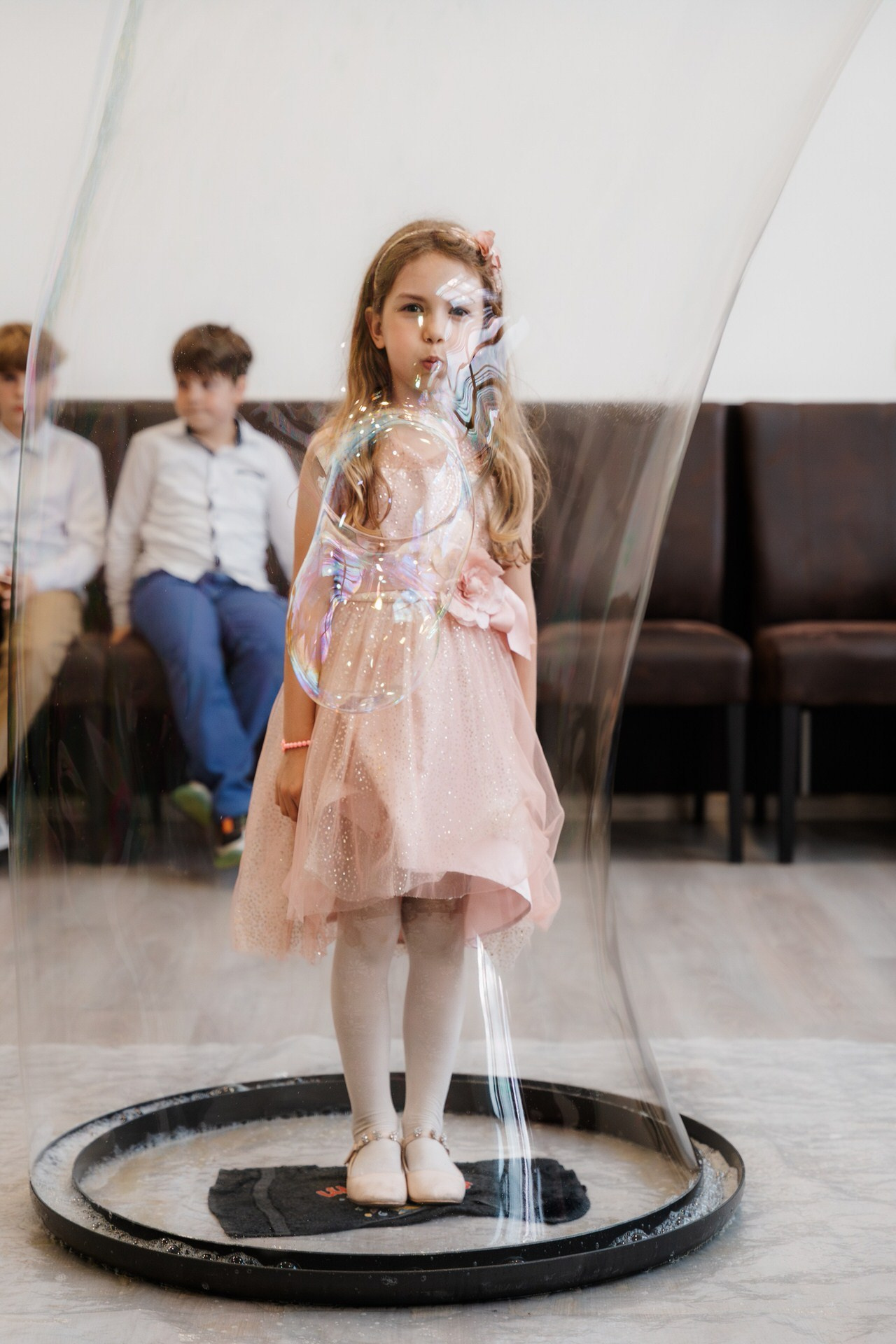 Devojčica gleda u fotoaparat dok animator postavlja balon od sapunice preko nje cele.