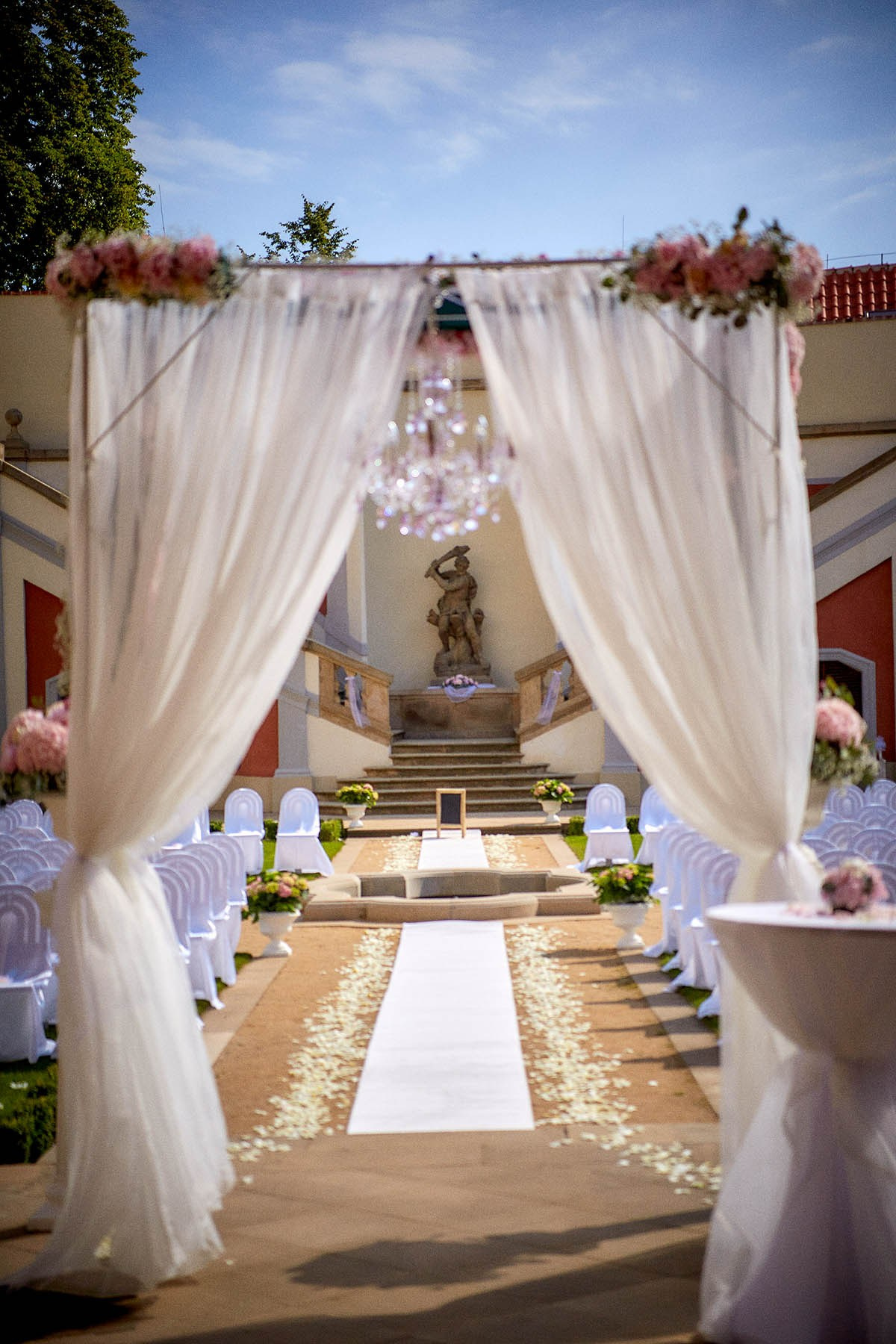 A view of the floral arch, hanging chandelier, and white curtains that frame the chandelier.
