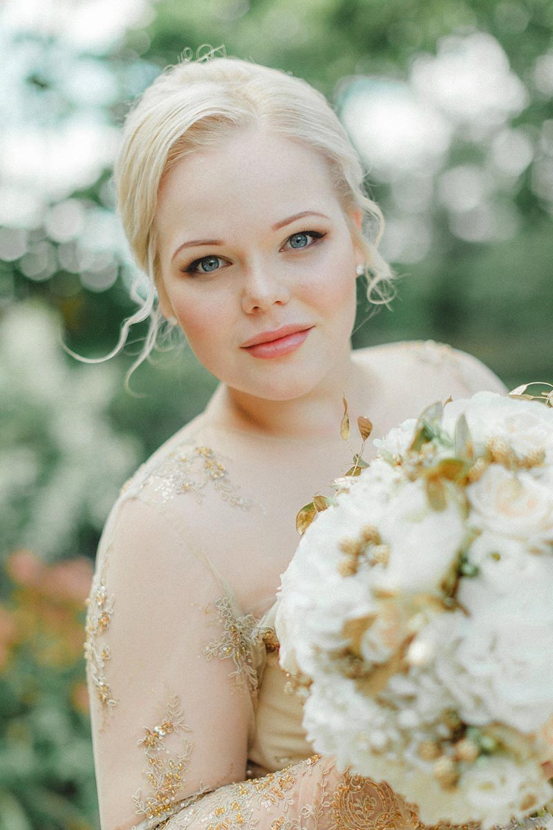 Light & Airy style bridal portrait of a blonde-haired bride holding a bouquet in a garden setting at the Chateau Mcely during her wedding day.