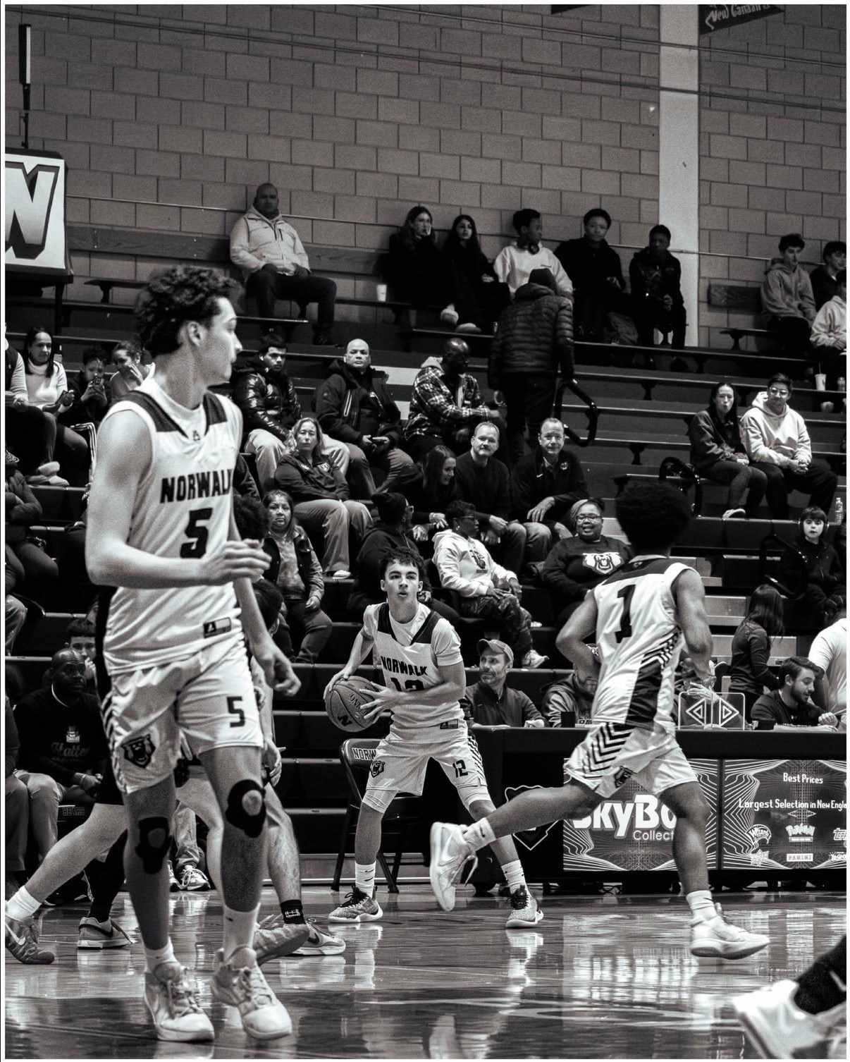 Black and white basketball action photo of players moving through a crowded gym court.