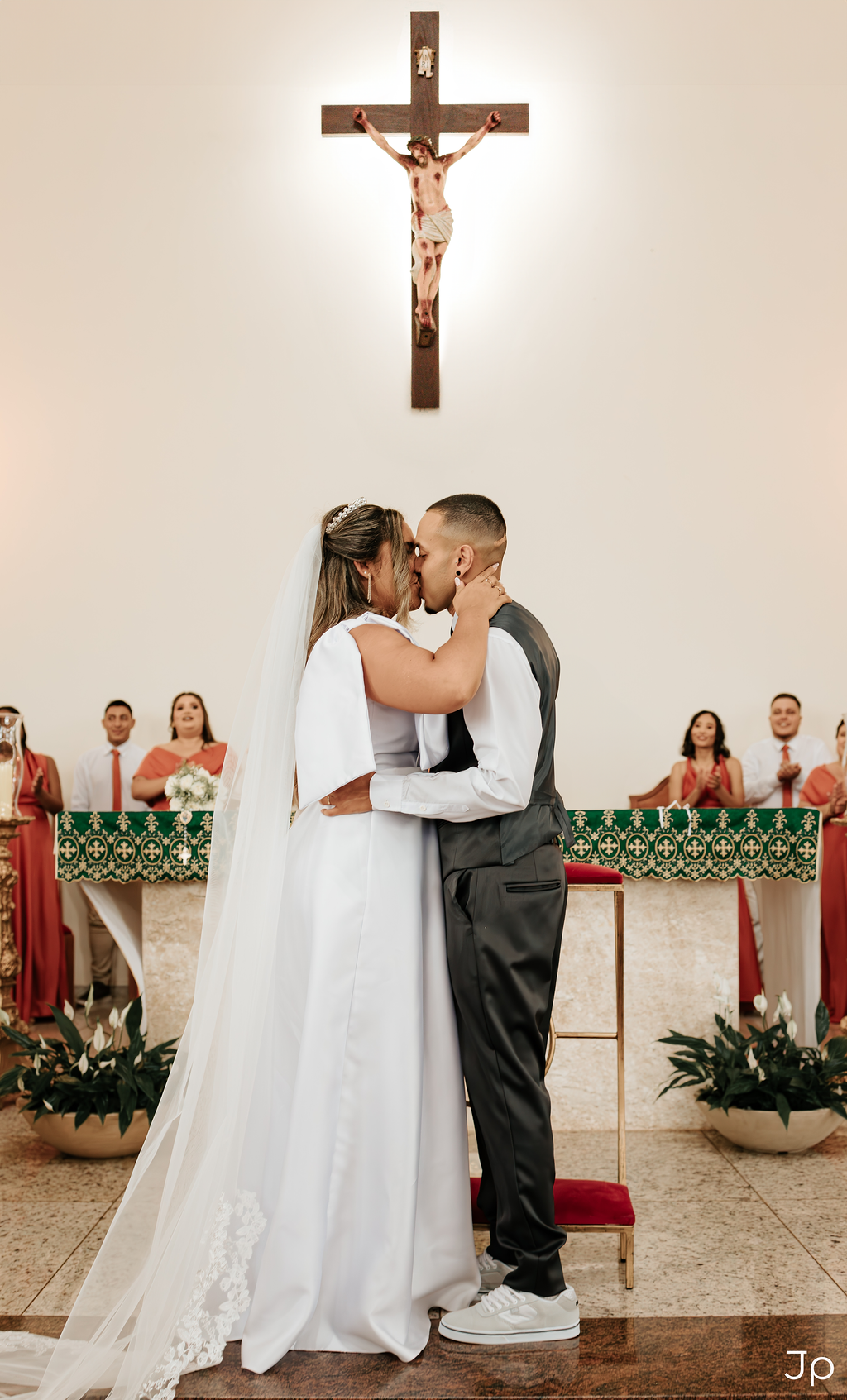 Casal se beija diante do altar com cruz após cerimônia.