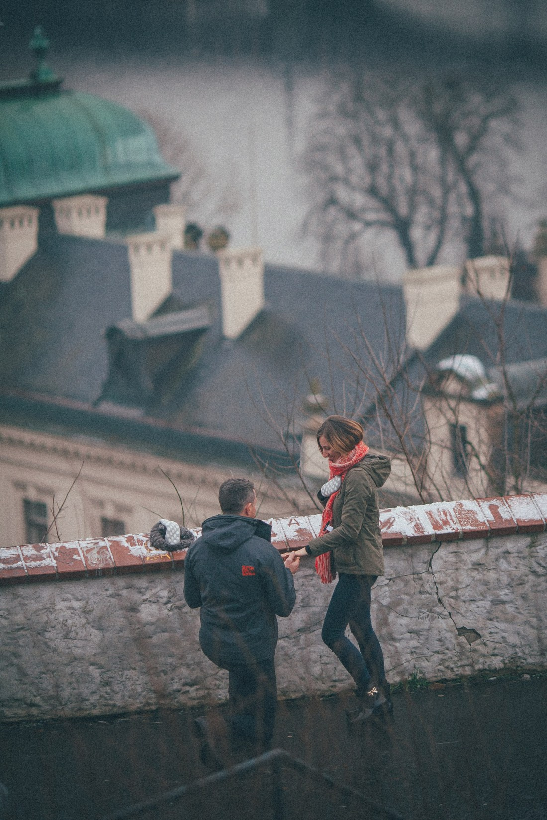 Birds-eye view of man proposing on knee placing diamond ring on partner’s finger in snowy Prague.