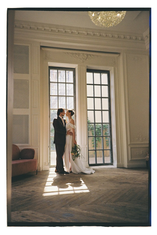 Bride and groom standing by window during editorial wedding portraits